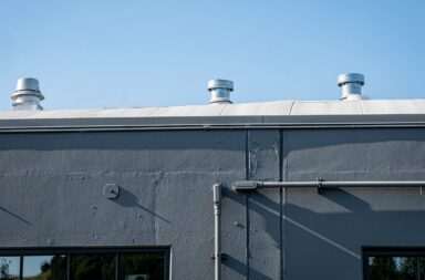 Exterior of a gray industrial building with rooftop vents under a clear blue sky.