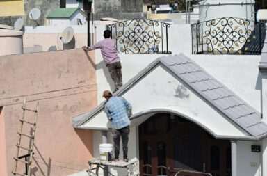 Two workers engaged in painting and renovating a building roof, showcasing a construction scene.