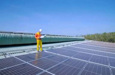 A solar technician inspects solar panels on a rooftop under a clear blue sky, promoting renewable energy.